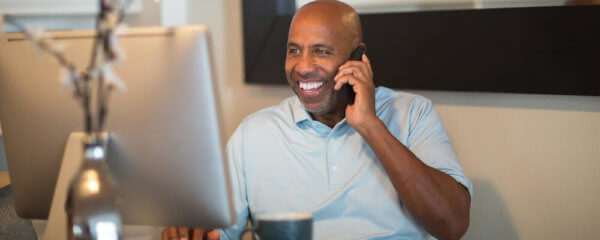 Man talking on his phone looking at his computer talking through hybrid workplace pros and cons