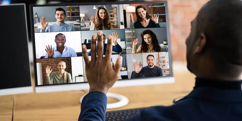 Back of man looking at computer raising his hand, post-pandmic work employees on computer video call with hands raised