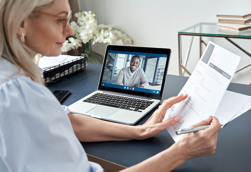 Woman looking at resume while conducting post-pandemic interview with man on video chat on the laptop