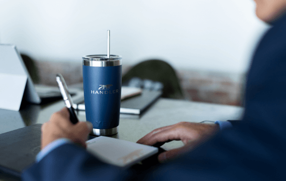 Handler recruiting sitting at table writing with a Handler cup.