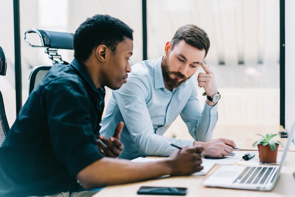 Two guys sitting at a work desk looking at a laptop talking about reskilling and upskilling employees