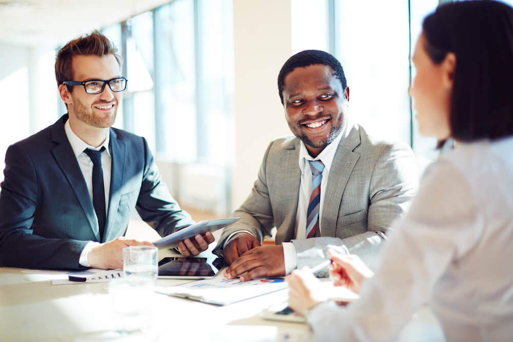 Two men and a woman at a table discussing hiring challenges at the end of the year